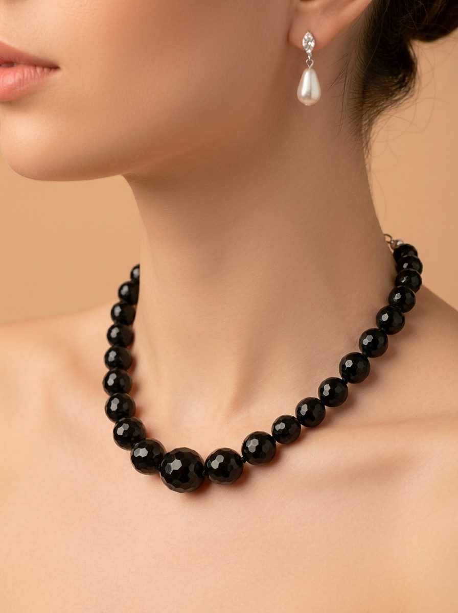 Close-up of black graduated bead necklace worn on a woman's neck paired with white pearl drop earrings