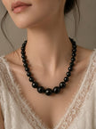 Black graduated bead necklace worn on a woman in a white lace top showing full neckline drape