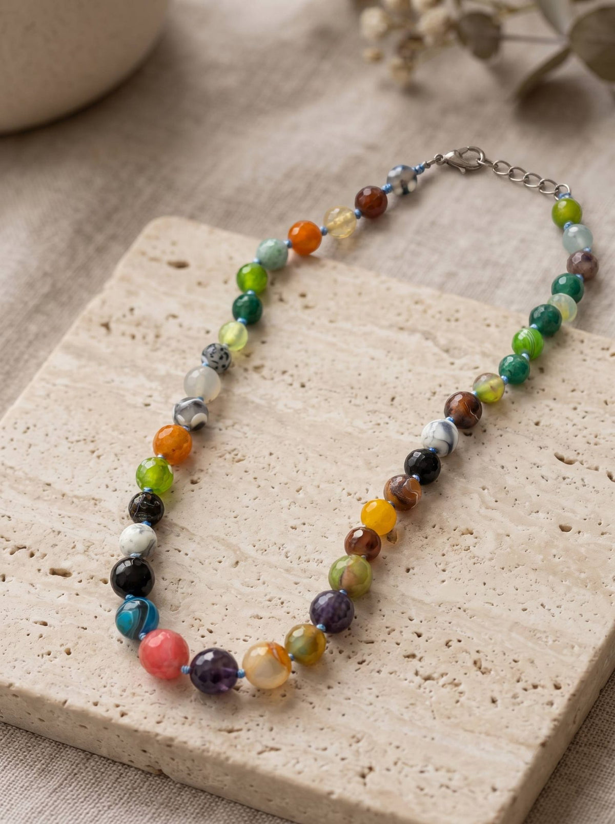 Multicolour round stone bead necklace laid flat on a travertine tile with lobster clasp visible