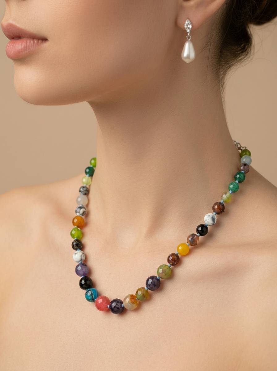 Model wearing multicolour beaded stone necklace at collarbone with pearl drop earrings on neutral background