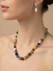 Model wearing multicolour beaded stone necklace at collarbone with pearl drop earrings on neutral background