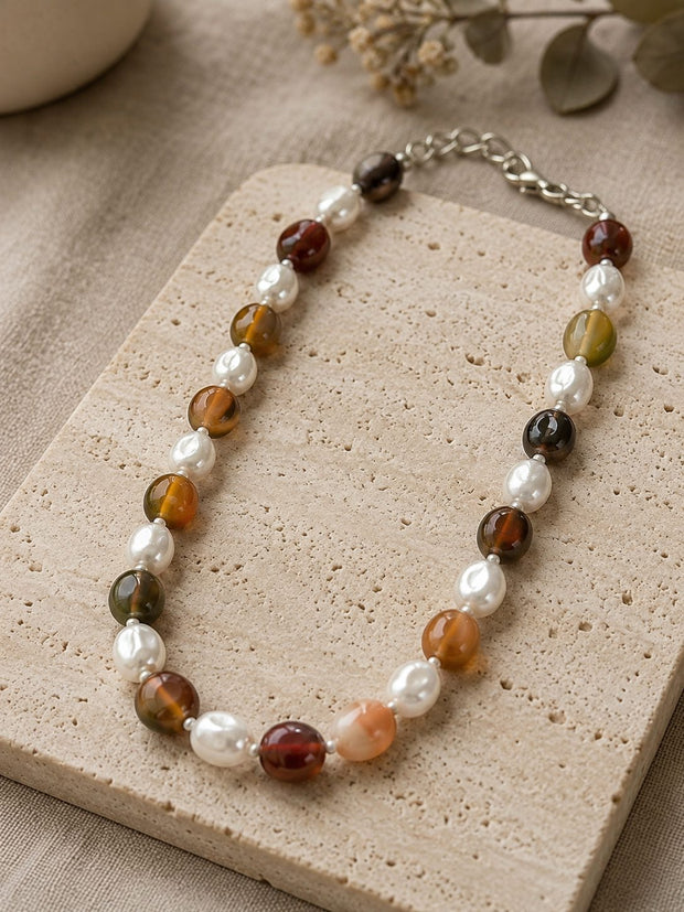Agate and baroque pearl beaded choker necklace laid flat on a textured travertine tile with dried botanicals in the background