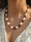 Close-up of agate and pearl choker necklace worn on a woman's neck over an embroidered white ethnic top in warm sunlight