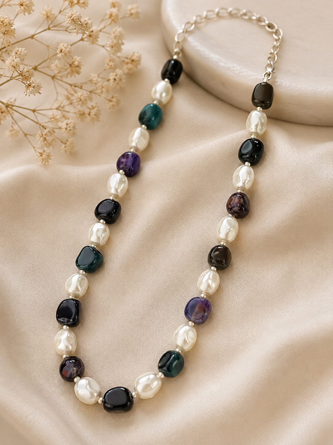 Baroque pearl and mixed stone beaded necklace laid flat on cream satin fabric with dried flowers