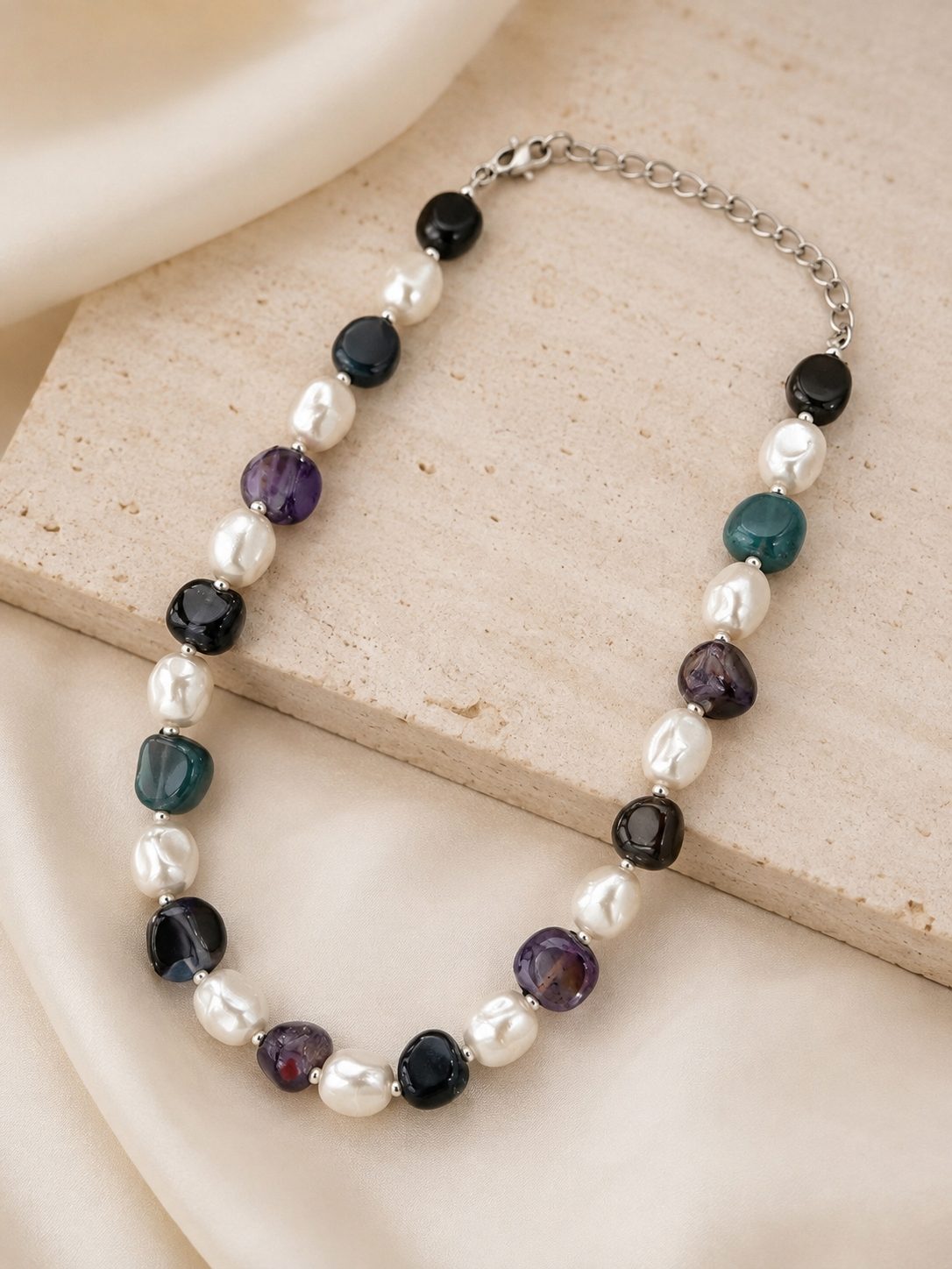 Closeup of pearl and multi-stone beaded necklace with silver-tone chain clasp on a stone surface