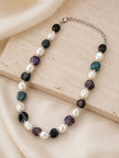 Closeup of pearl and multi-stone beaded necklace with silver-tone chain clasp on a stone surface