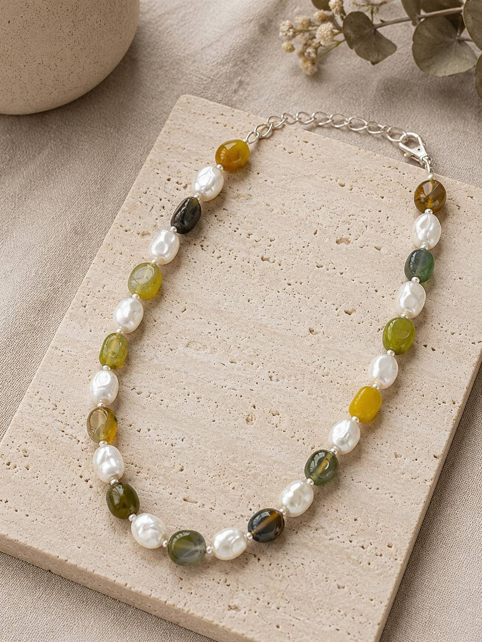 Green agate baroque pearl necklace displayed on a travertine stone tile with eucalyptus in the background