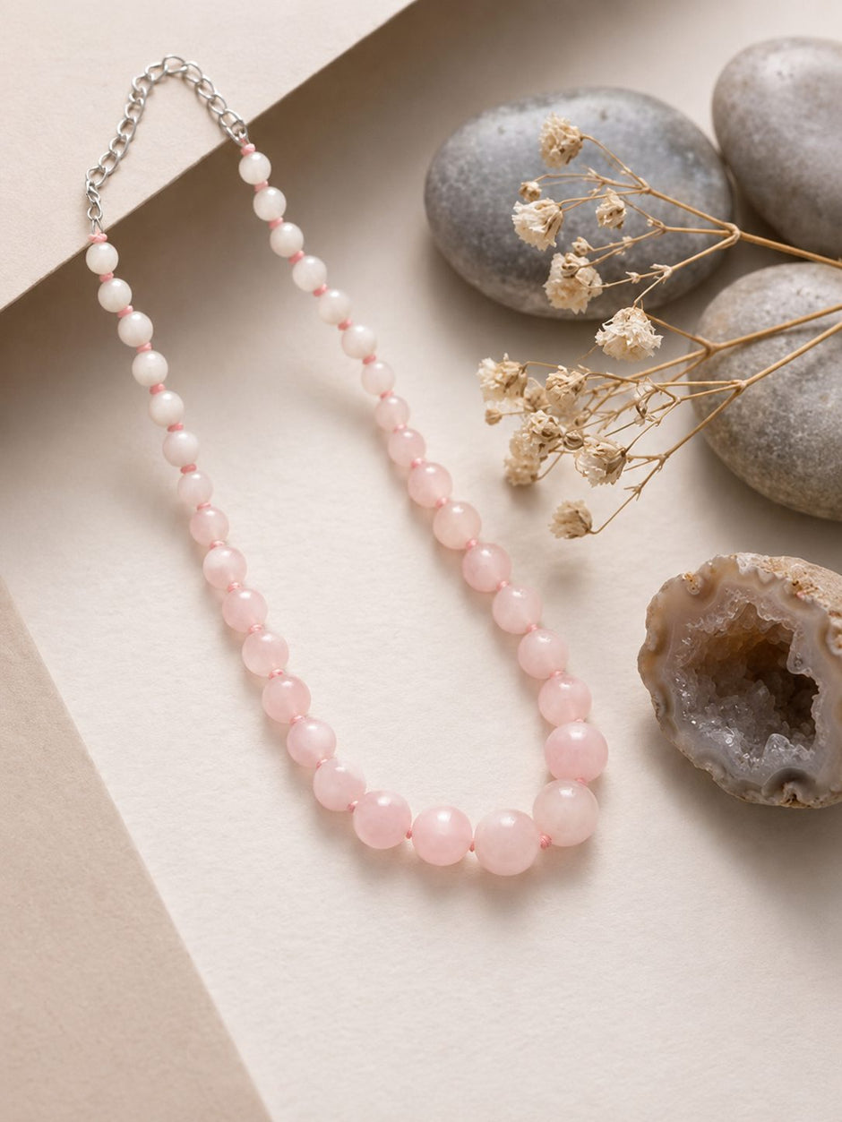 Rose quartz ombre bead necklace laid flat on cream paper with smooth pebbles and dried flowers beside it