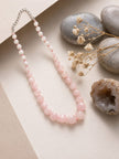 Rose quartz ombre bead necklace laid flat on cream paper with smooth pebbles and dried flowers beside it
