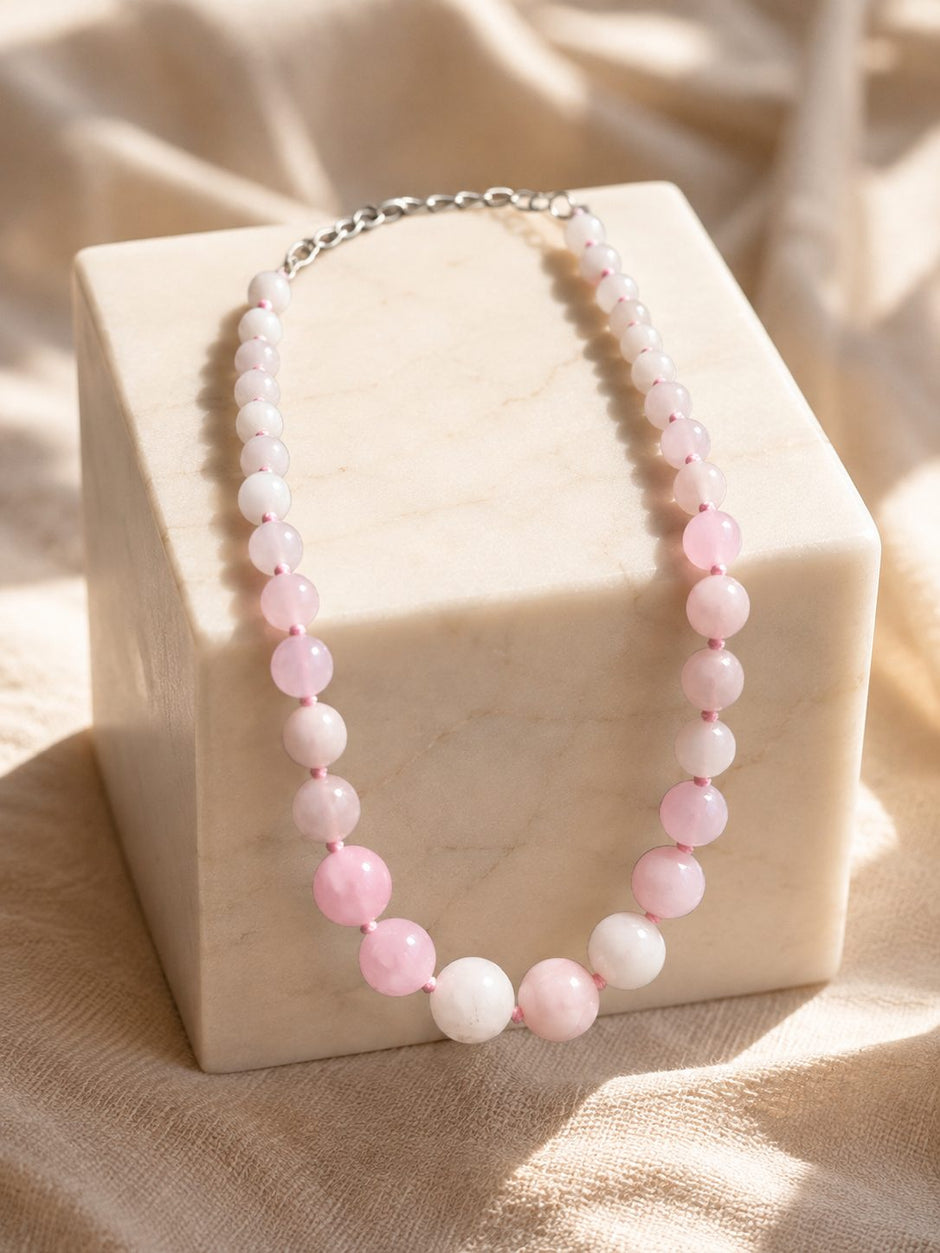 Pink and white quartz bead necklace draped over a marble cube block in warm natural light