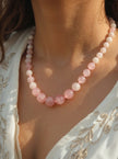 Rose quartz bead necklace worn around a woman's neck over a white embroidered top in sunlight