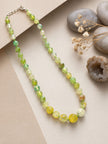 Green and yellow agate beaded necklace laid flat on beige paper beside smooth pebbles and dried flowers