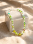 Yellow and green agate necklace draped over a white marble cube on a textured linen surface