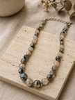 Grey and cream faceted bead graduated necklace laid flat on a travertine stone tile with dried flowers
