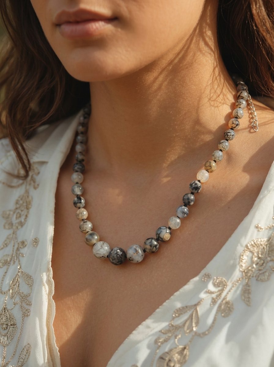 Graduated grey stone bead necklace worn around a woman's neck over a white embroidered kurta outdoors