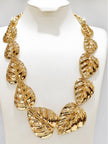 Gold-plated monstera leaf statement necklace displayed on a white jewellery bust, showing full graduated leaf arrangement