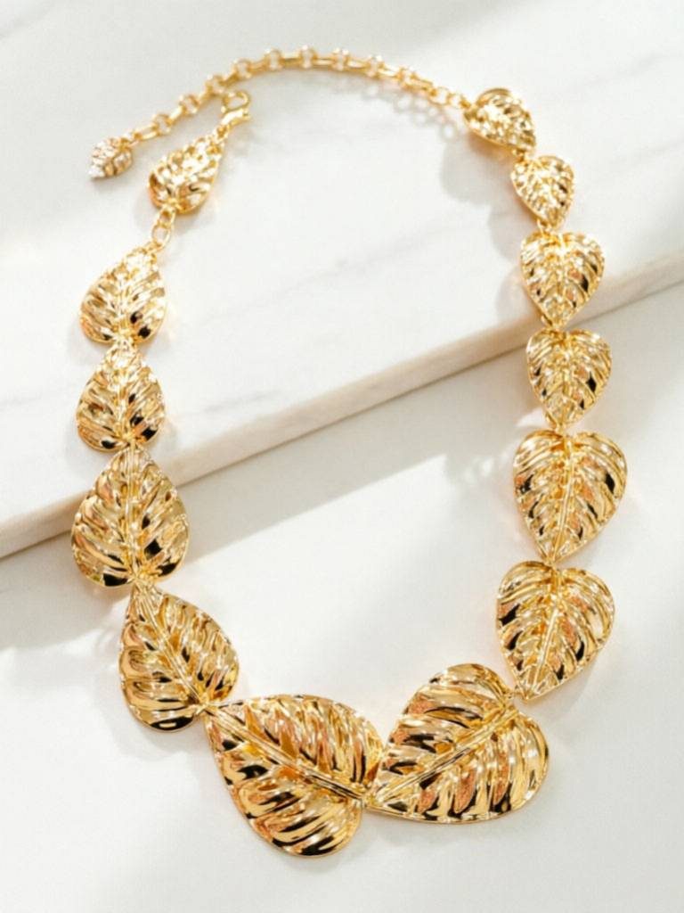 Gold monstera leaf necklace laid flat on a white marble surface showing adjustable lobster clasp chain