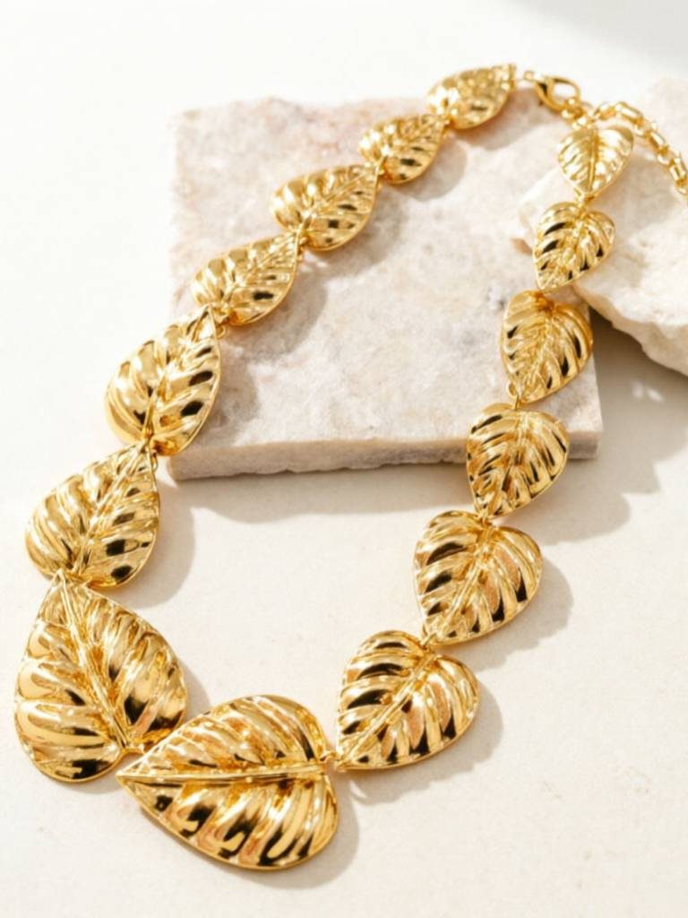 Gold leaf statement necklace arranged in a loop on a white stone surface showing full length and leaf sizing