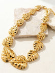 Gold leaf statement necklace arranged in a loop on a white stone surface showing full length and leaf sizing