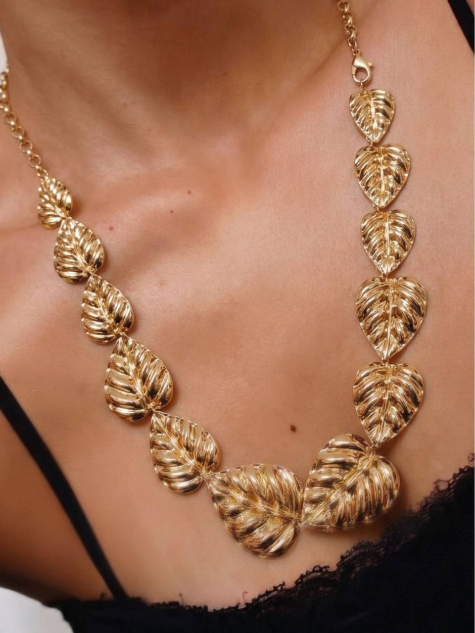 Gold-plated monstera leaf necklace worn around a woman's neck against a black top showing fit and scale