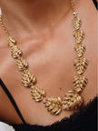 Gold-plated monstera leaf necklace worn around a woman's neck against a black top showing fit and scale