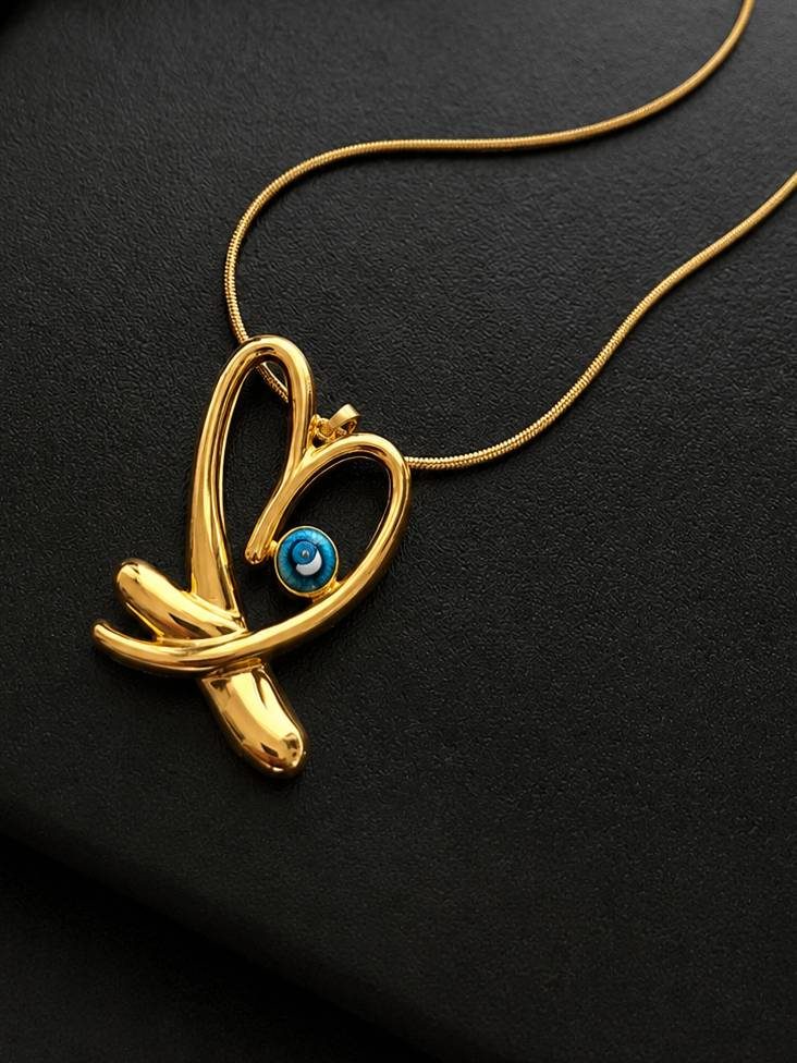 Close-up of gold sculptural heart pendant with blue evil eye cabochon on a black surface