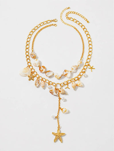 Flat lay of a double-layer gold-tone necklace with spiral shell beads, conch shell charms, faux pearl drops and a dangling starfish pendant on white background