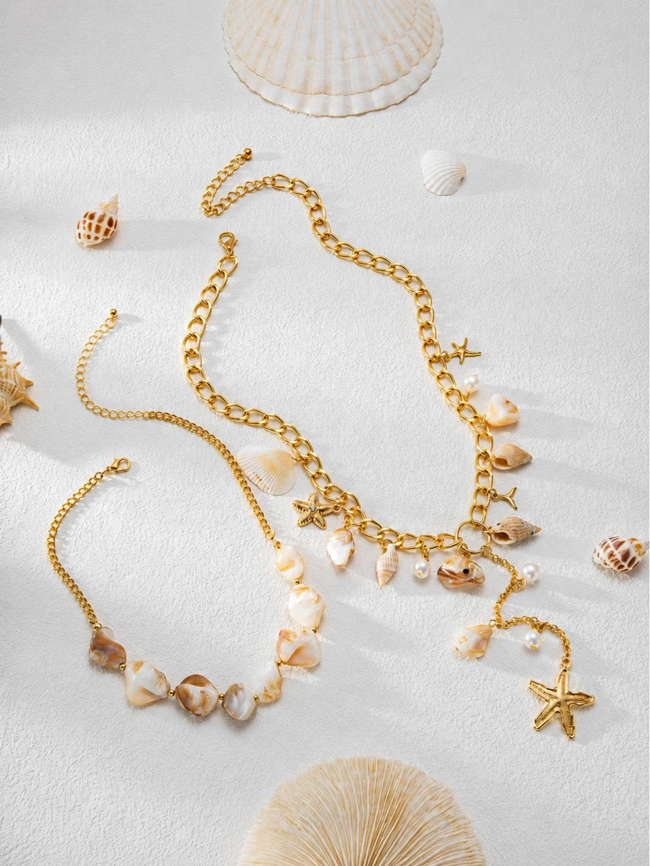 Two gold-tone seashell necklaces laid separately among scattered seashells and coral on a white textured surface