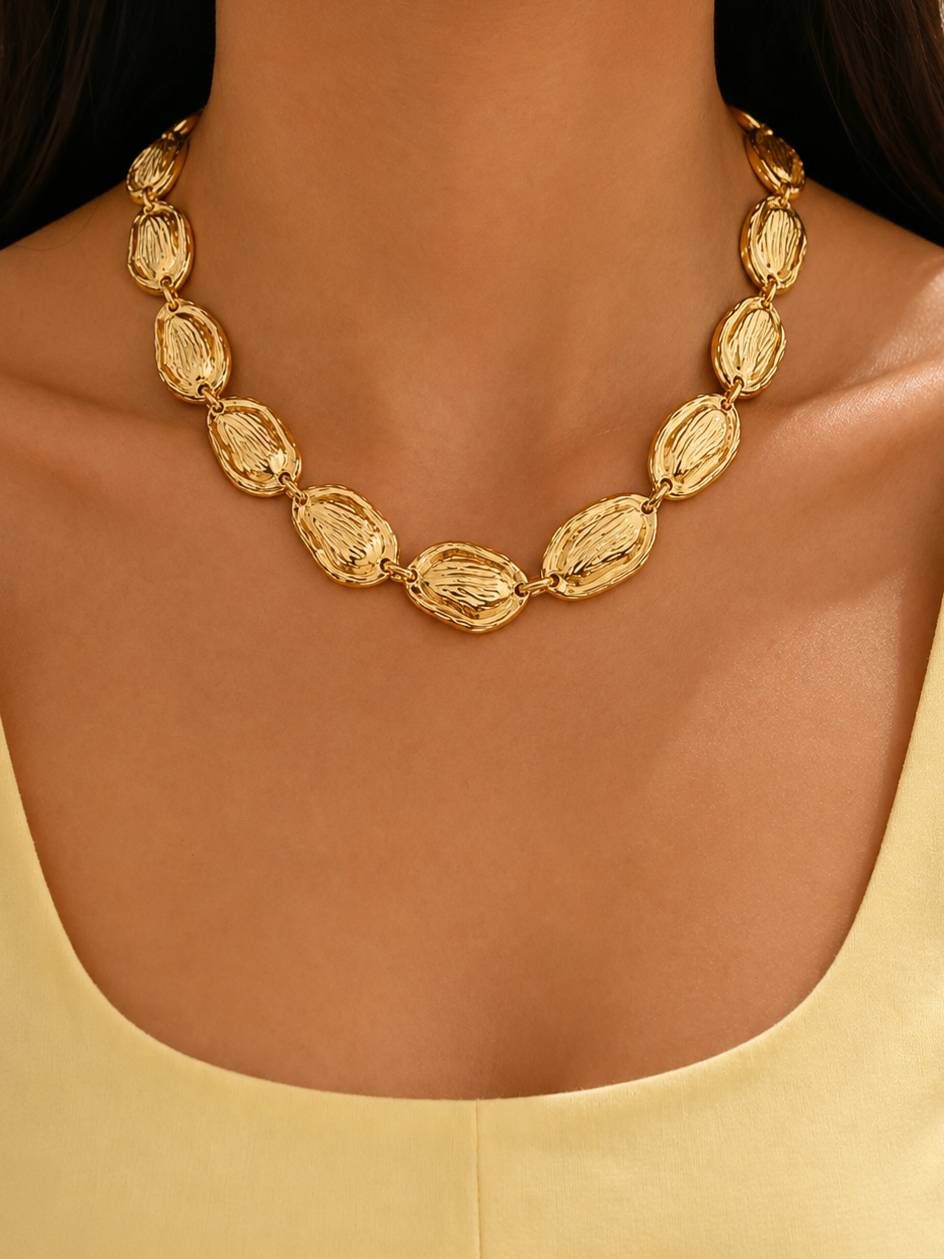 Model wearing gold-plated oval link necklace over a yellow top, collarbone view