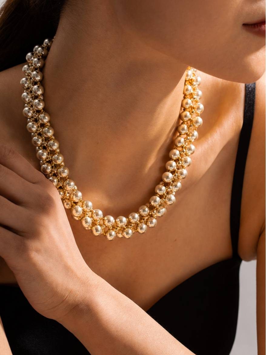 Gold ball cluster necklace worn around a model's neck over a black dress showing fit at the collarbone