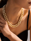 Gold ball cluster necklace worn around a model's neck over a black dress showing fit at the collarbone