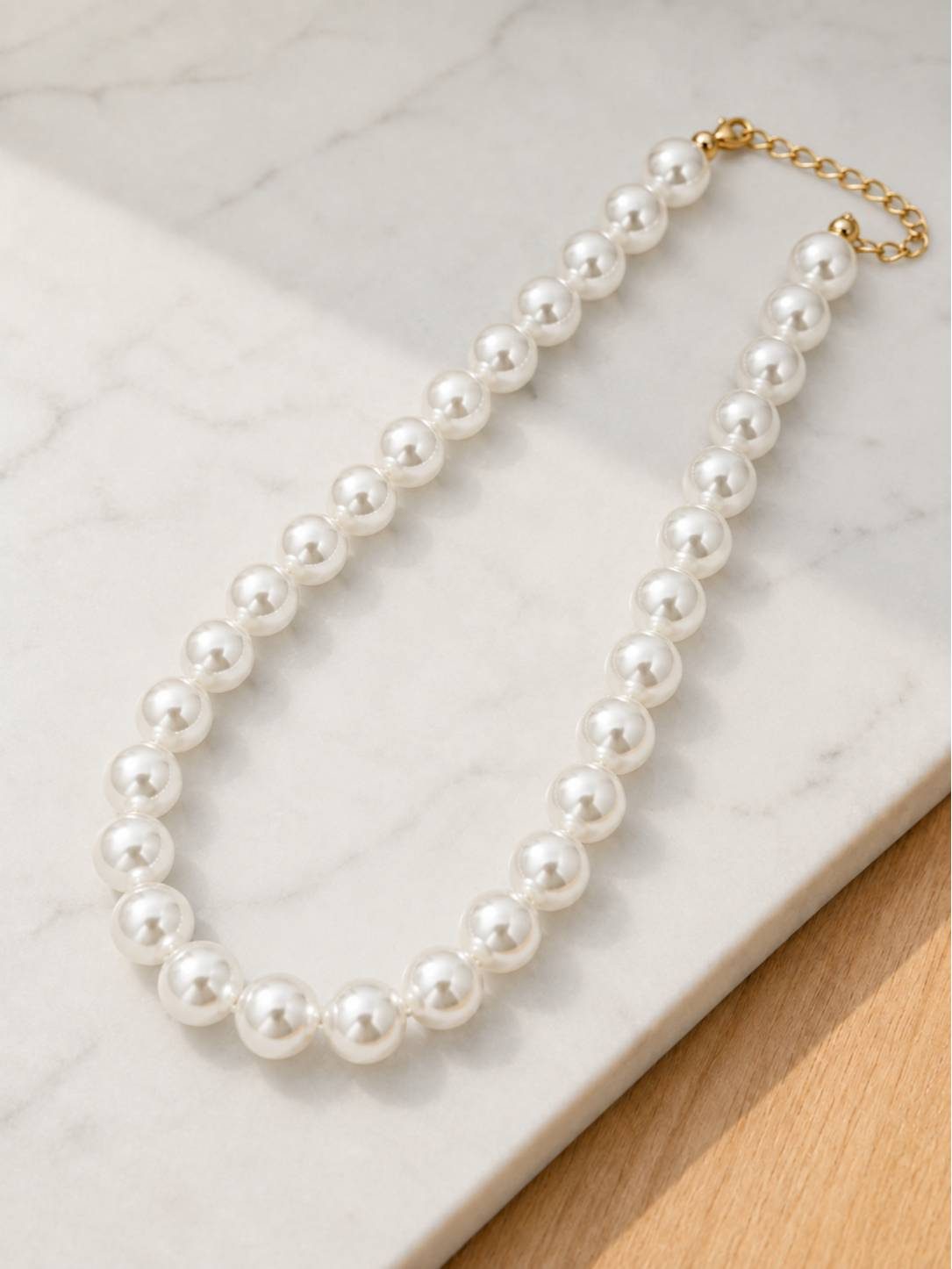 White pearl choker necklace laid on a white marble surface showing gold-tone lobster clasp and extender chain