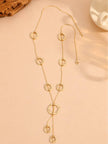Gold-plated circle charm lariat necklace laid flat on a beige surface showing all nine rings and Y-drop pendant