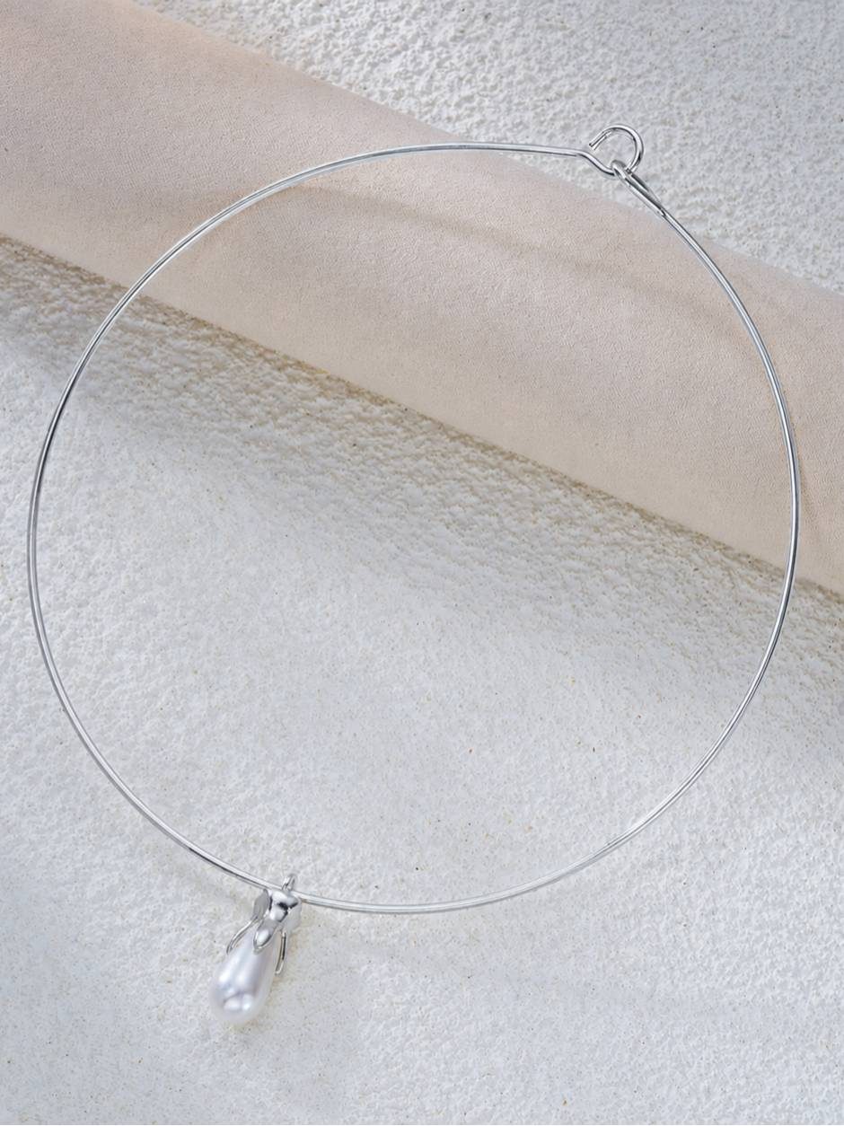 Silver wire choker necklace with sculpted faux pearl teardrop pendant laid flat on white textured surface