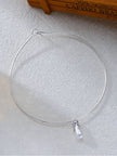 Top view of silver rigid hoop choker with pearl drop pendant beside a wooden coffee box on white background