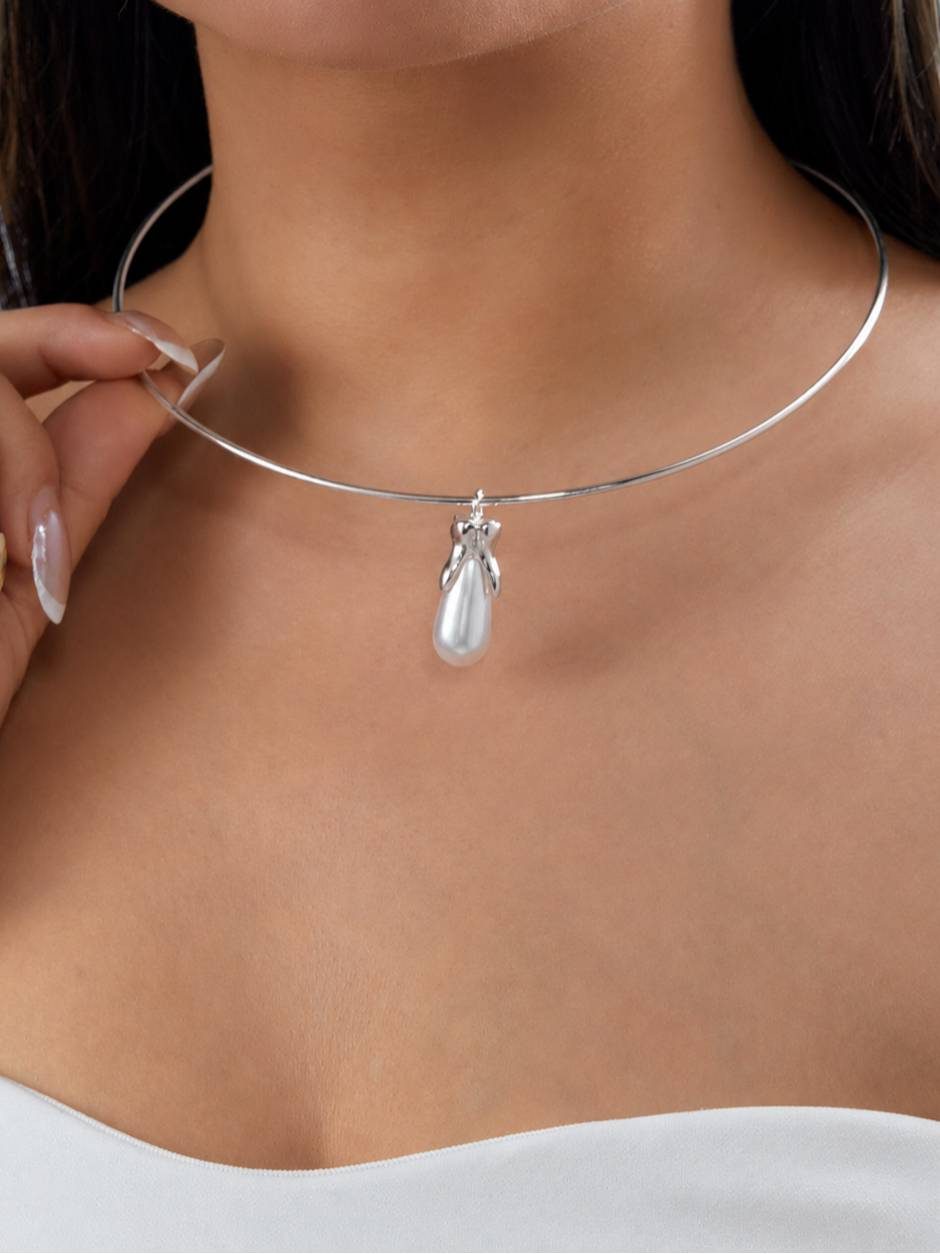 Model wearing silver wire choker with pearl pendant, holding the open end at her neck over a white top