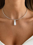 Close-up of silver wire choker with baroque faux pearl drop pendant resting at model's collarbone