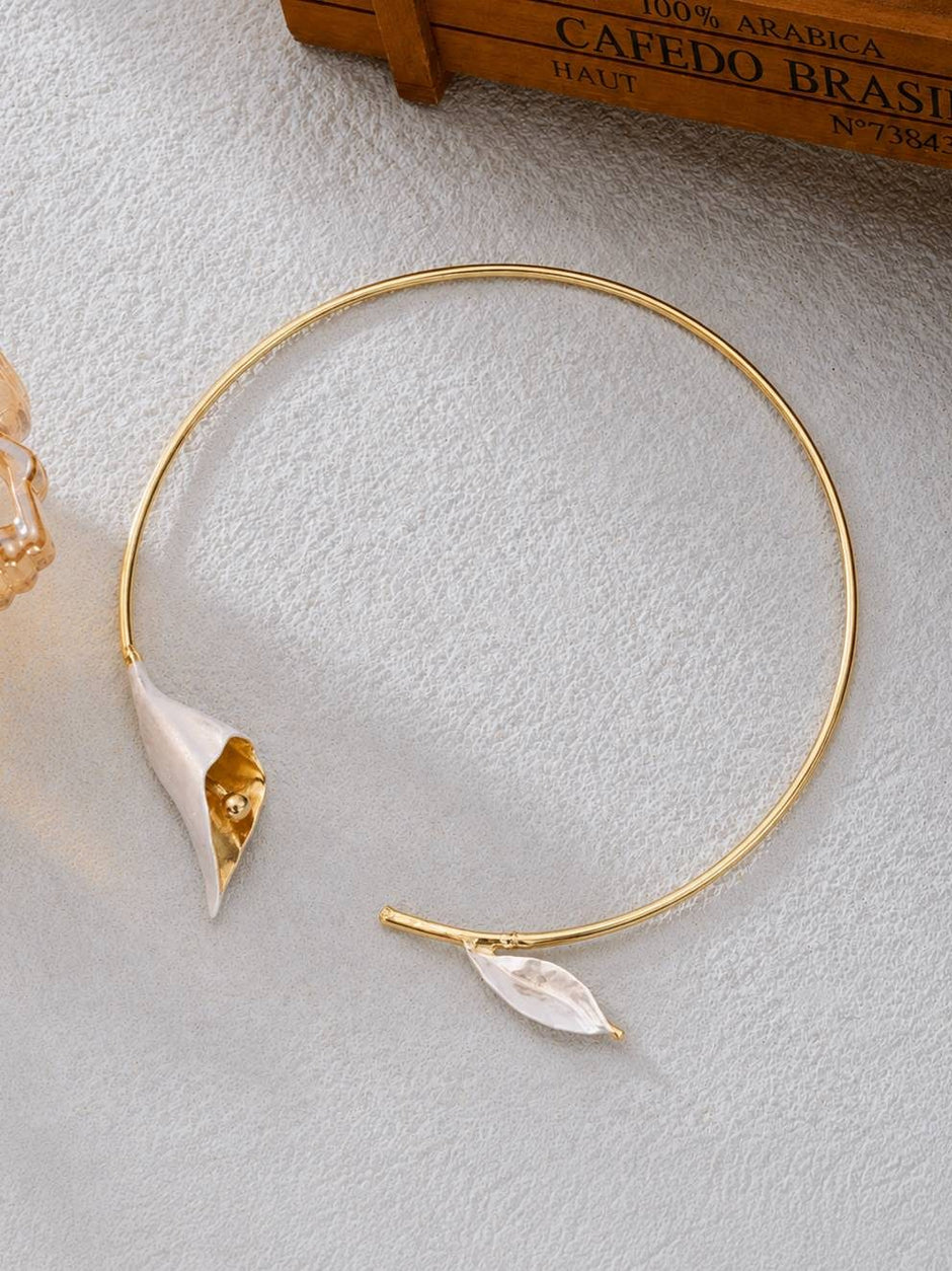 Flat lay of gold collar choker necklace with calla lily bloom and small leaf end on a white textured surface
