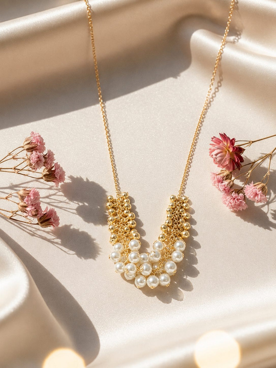 Gold-plated pearl cluster necklace laid flat on cream satin with small dried pink flowers around it