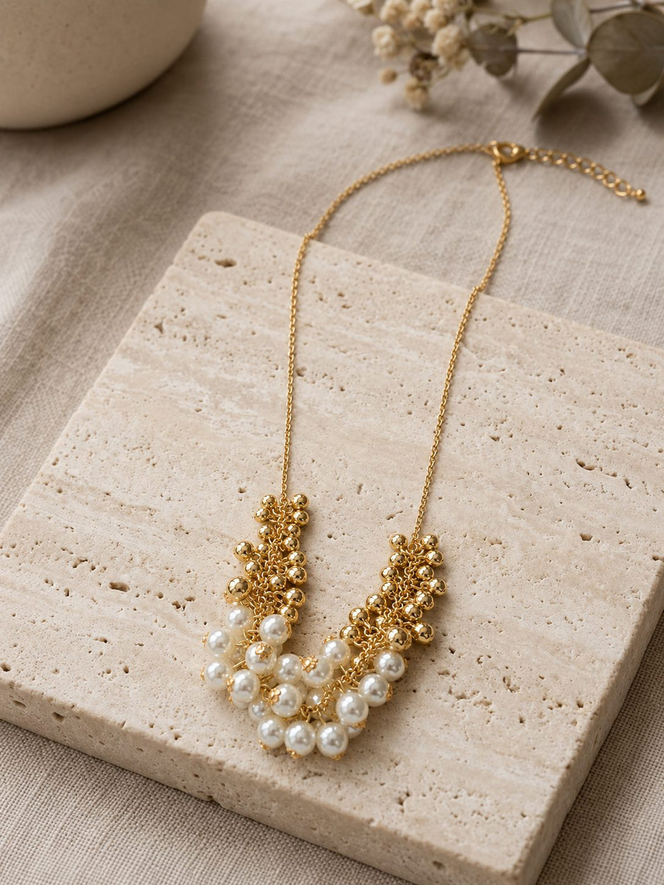 Pearl and gold bead cluster necklace displayed on a travertine stone tile with eucalyptus sprigs in background