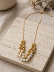 Pearl and gold bead cluster necklace displayed on a travertine stone tile with eucalyptus sprigs in background