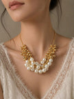 Model wearing gold-plated faux pearl cluster necklace over a white lace top showing collarbone drape