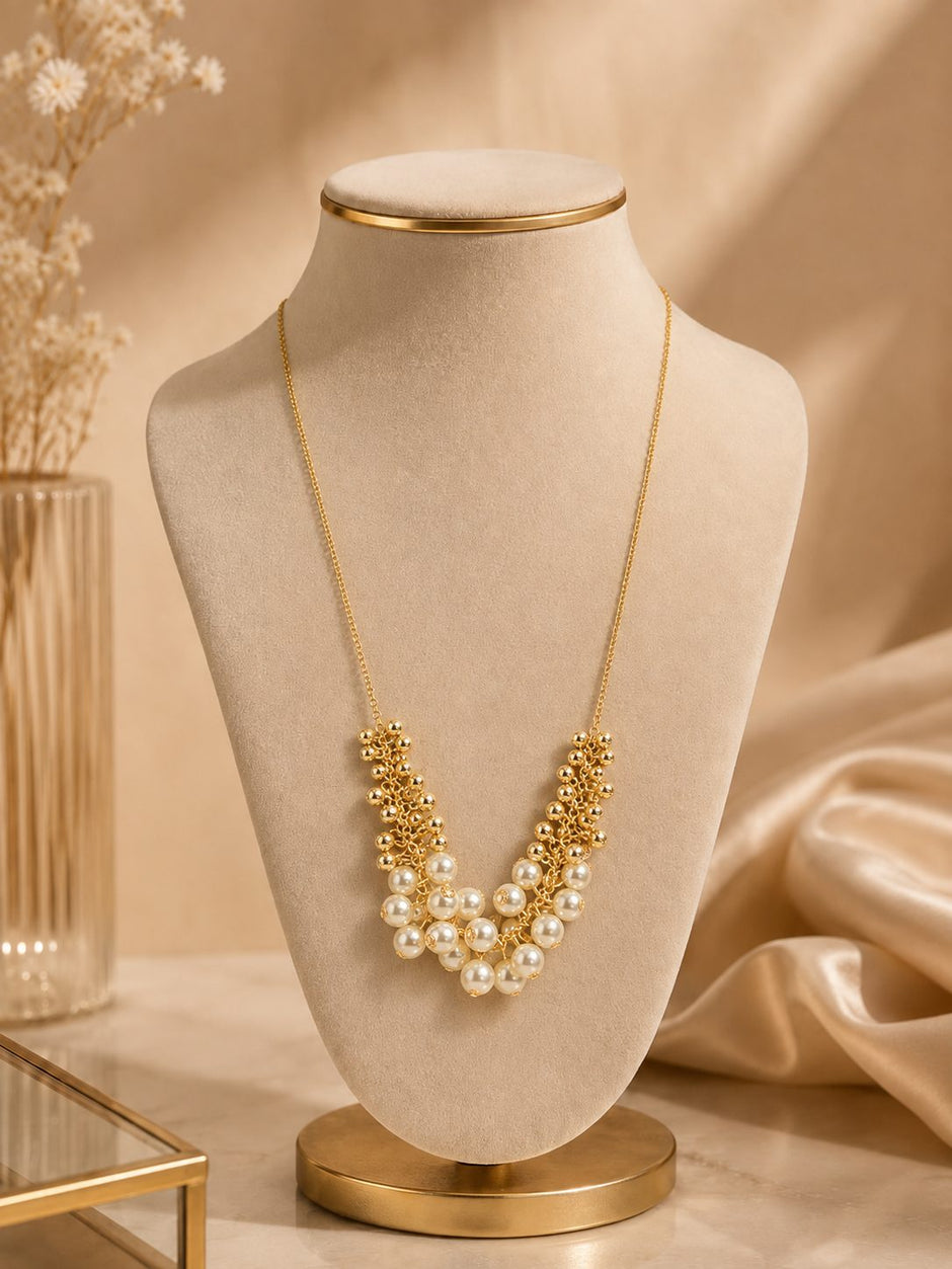 Gold-plated pearl cluster statement necklace on a beige velvet jewellery bust with gold satin fabric backdrop