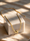 Gold snake chain necklace with sliding knot pendant draped over a white marble block