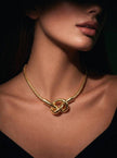 Model wearing gold knot pendant necklace on a snake chain against a dark background