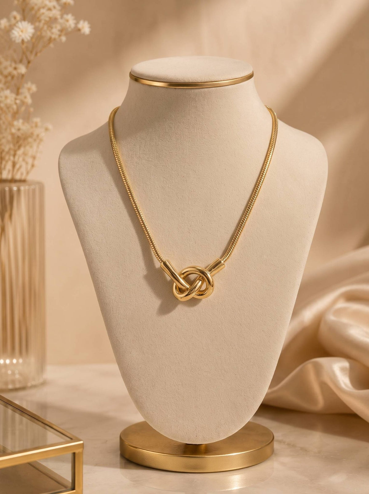 Gold knot necklace displayed on a beige velvet jewellery bust with warm neutral backdrop