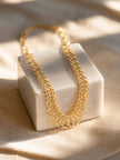 Gold chain necklace with graduated circular links draped over a white marble block in warm sunlight