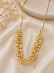Gold-plated spike drop necklace laid flat on cream satin fabric beside dried flowers