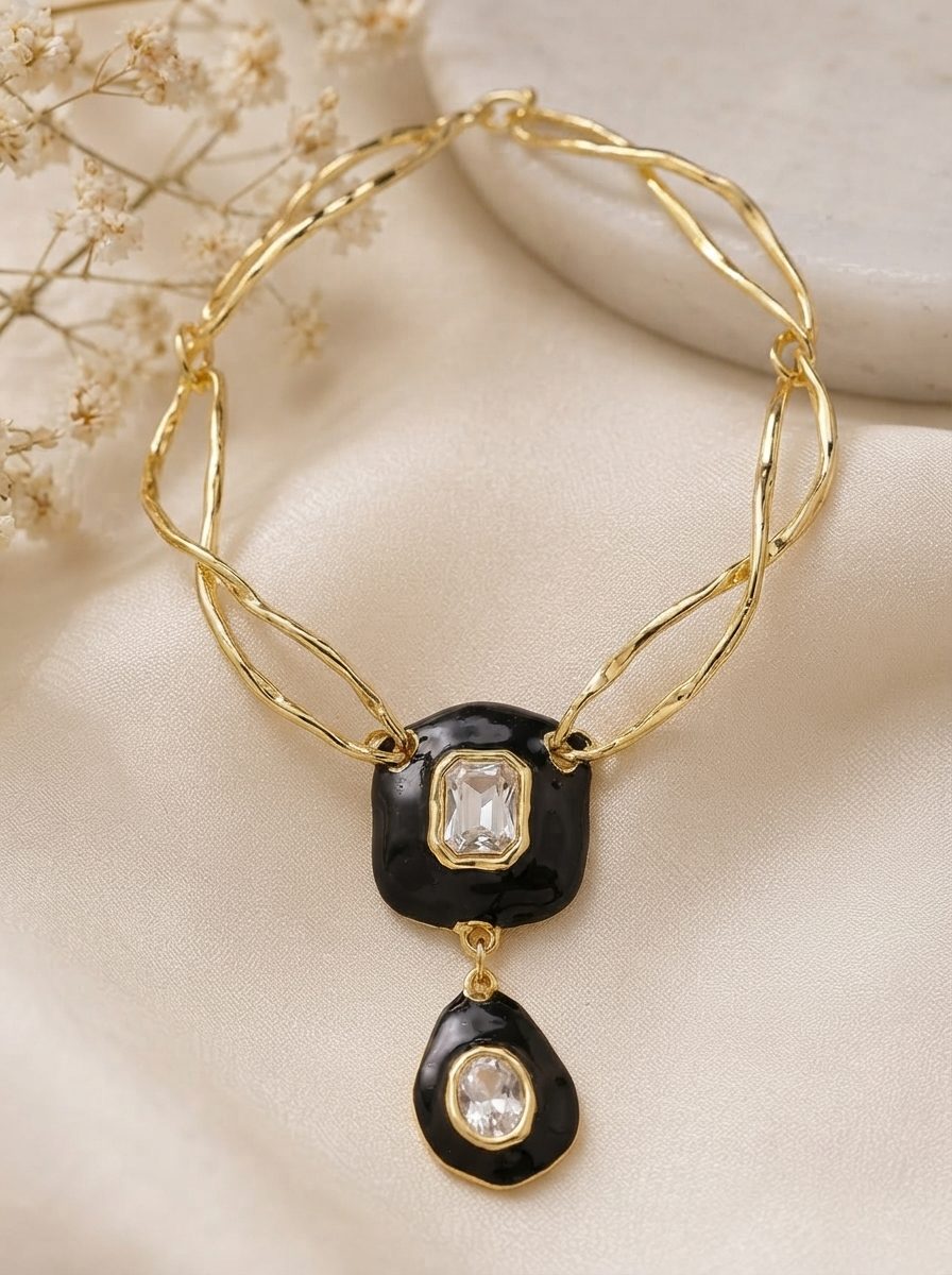 Gold-plated black enamel double pendant necklace with crystal centres laid flat on ivory silk fabric
