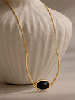Close-up of black oval bezel pendant with curved gold bar links against a textured stone bust
